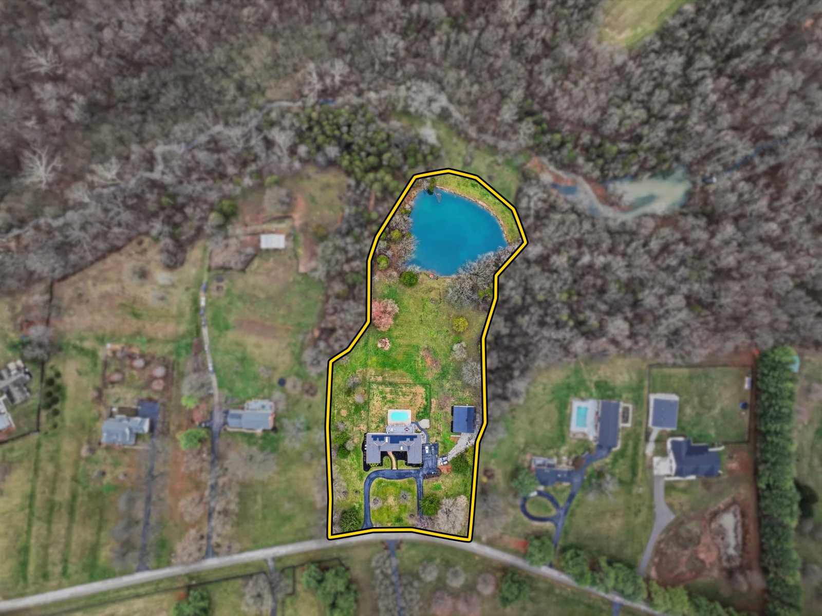 A drone photo with a yellow outline around a home, driveway, lawn, and pond, and softer, darker surroundings